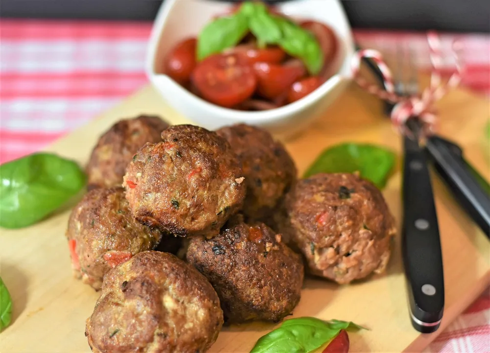 Oven baked meatballs on a board with basil and cherry tomatoes, showing how long to cook meatballs in oven