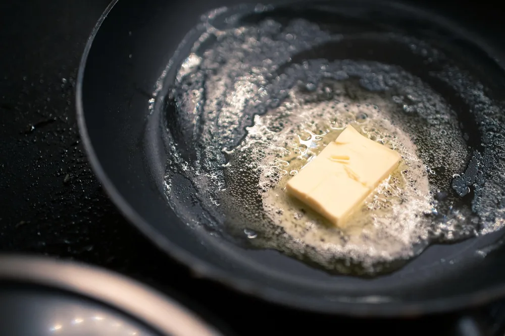 A pat of butter melting and foaming in a hot black skillet, ready for basting