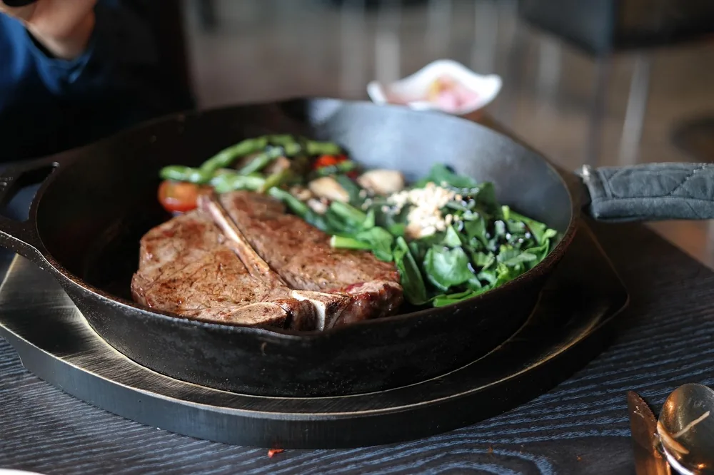 Cast iron skillet steak, a seared T-bone with spinach and mushrooms in the pan