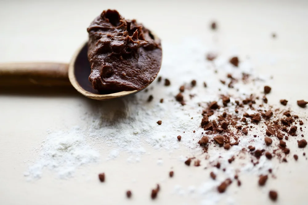 Spoonful of chocolate with cocoa crumbs and flour on a white table