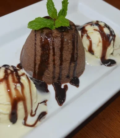 Single serve chocolate cake drizzled with chocolate sauce with vanilla ice cream and mint, like a chocolate mug cake turned out