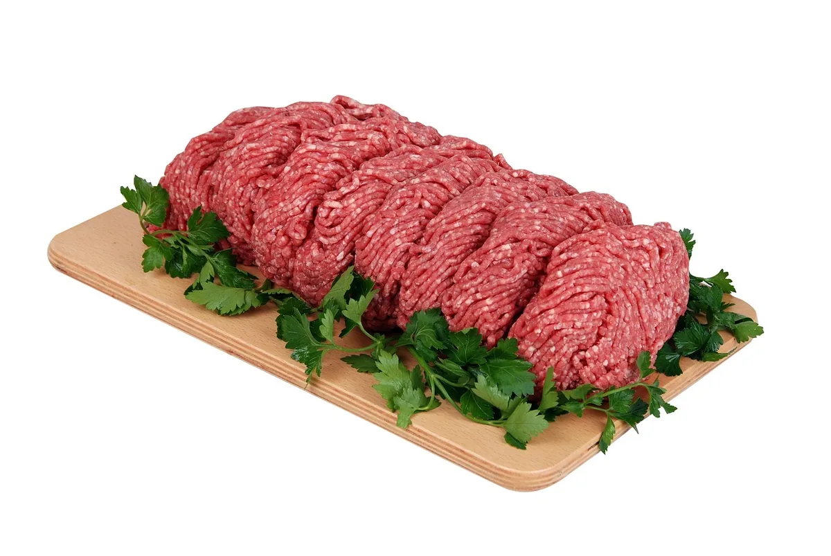 Fresh red ground beef on a wooden board with parsley, showing the bright color of oxygenated meat