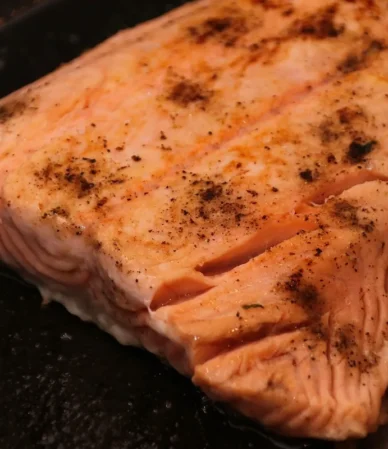 Salmon internal temp check: seared salmon fillet in a dark pan with opaque, flaking flesh
