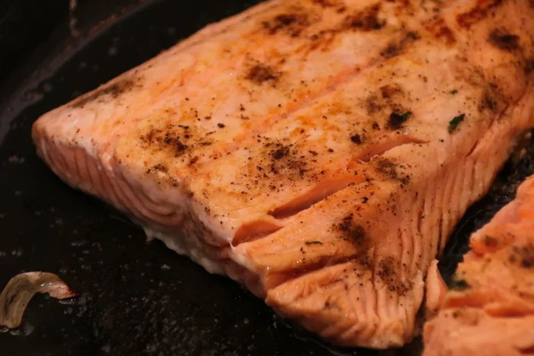Salmon internal temp check: seared salmon fillet in a dark pan with opaque, flaking flesh