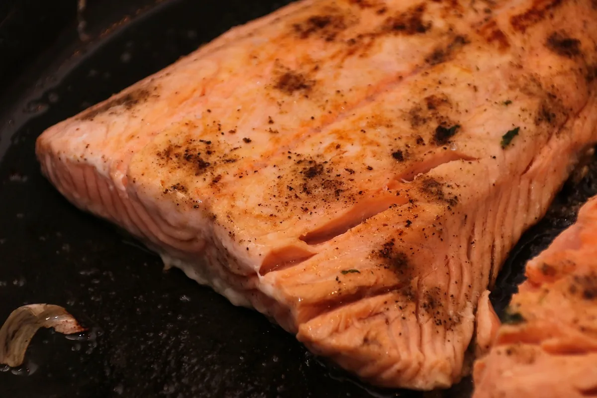 Salmon internal temp check: seared salmon fillet in a dark pan with opaque, flaking flesh