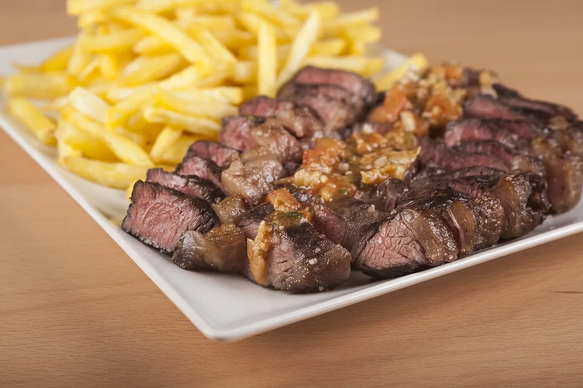 Grilled beef sliced thin against the grain with garlic, served with fries on a white plate