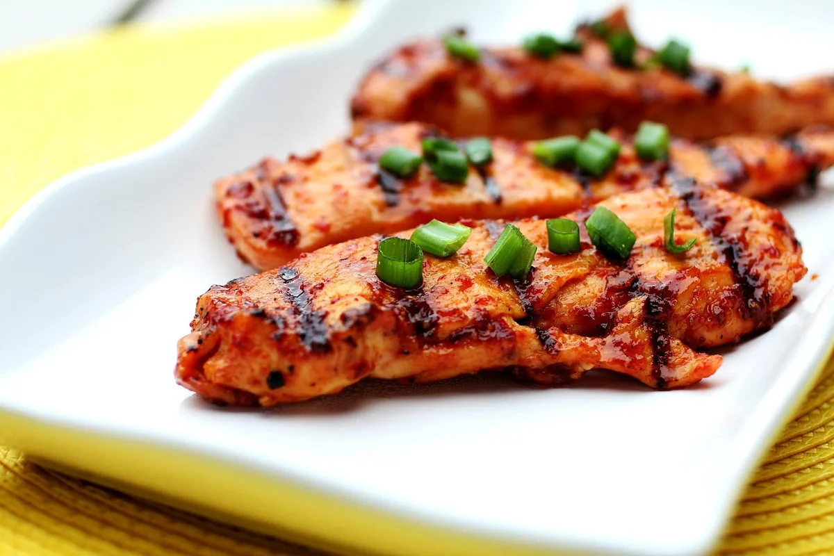 Strips of grilled chicken breast with a red glaze and green onions on a white plate