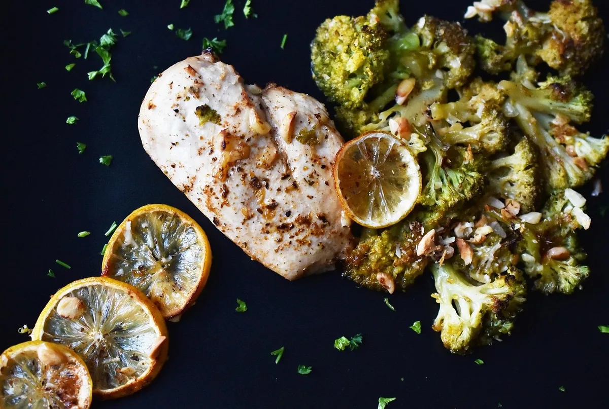 Baked chicken breast with roasted lemon slices and broccoli on a dark surface
