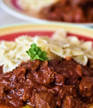 Beef in a rich brown sauce with parsley next to bow-tie pasta on a plate, similar to ground beef stroganoff