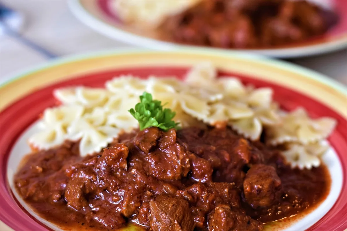 Beef in a rich brown sauce with parsley next to bow-tie pasta on a plate, similar to ground beef stroganoff