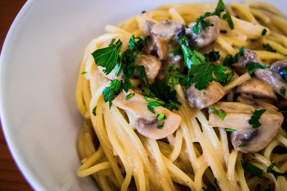 Pasta tossed with sliced mushrooms and fresh parsley in a white bowl