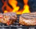 Two thick New York strip steak cuts searing on a grill grate with flames behind