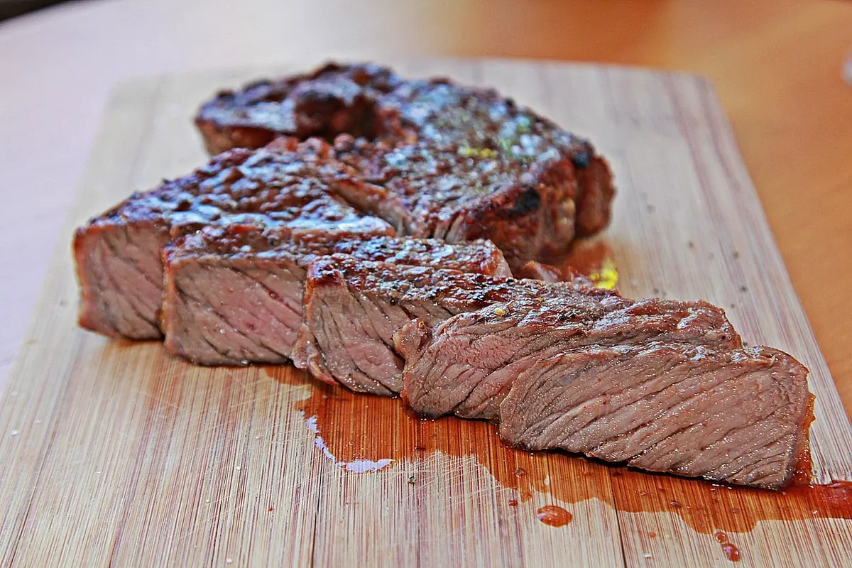 Grilled steak sliced across the grain on a wooden board, pink in the center