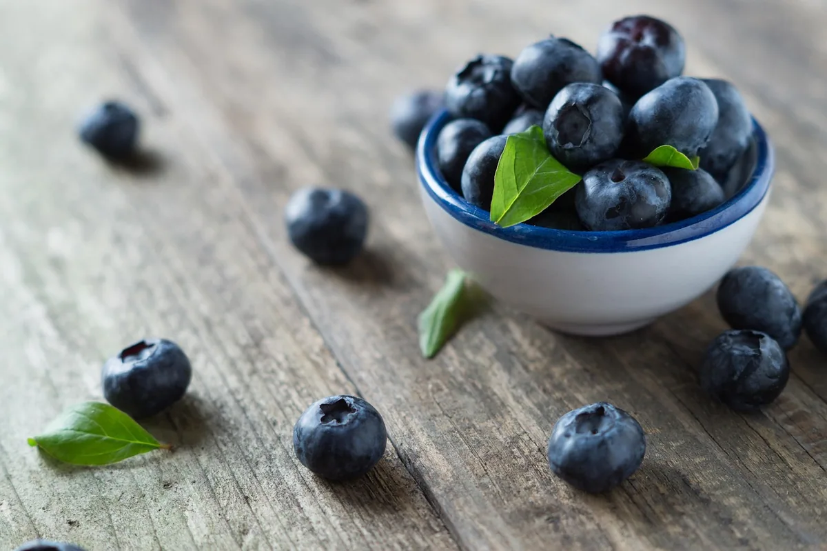 Fresh blueberries in a small white bowl on a rustic wooden table