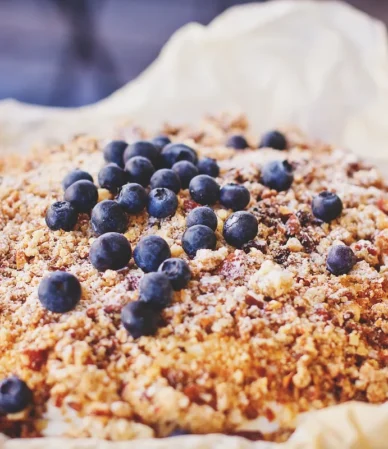 Baked blueberry dessert with a golden crumbly topping in a parchment-lined pan, similar to a blueberry dump cake