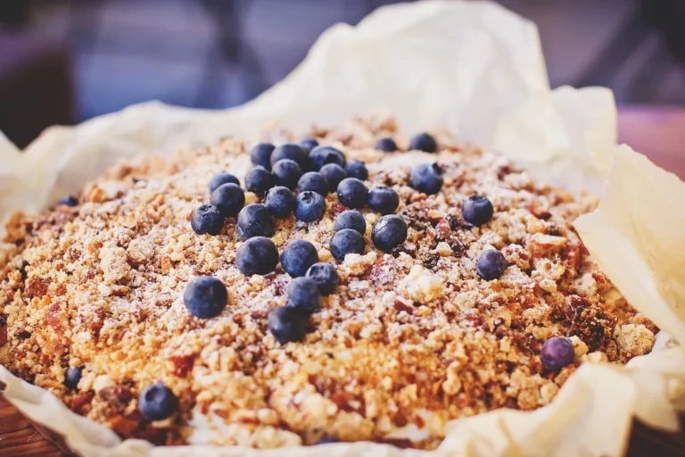 Baked blueberry dessert with a golden crumbly topping in a parchment-lined pan, similar to a blueberry dump cake