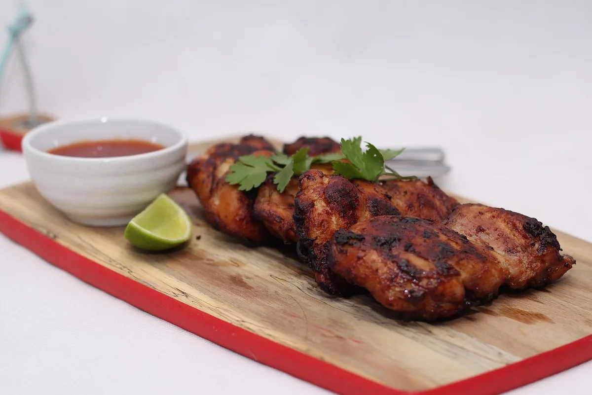 Smoky, charred chicken thighs on a wooden board with lime and a dipping sauce, similar to smoked chicken thighs