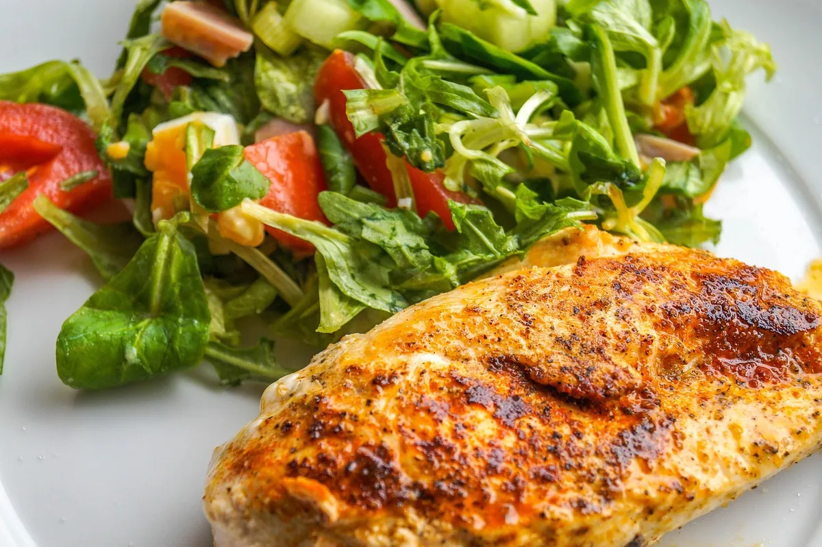 Golden paprika-seasoned baked chicken breast on a plate beside a fresh mixed green salad