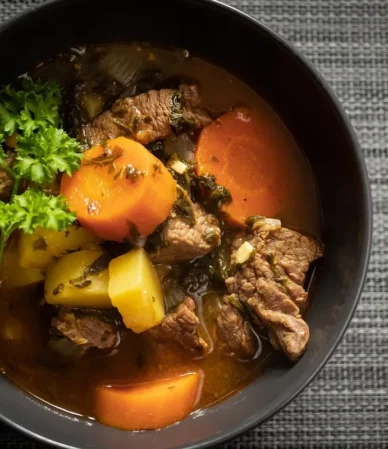Crockpot beef stew with tender beef, carrots and potatoes in a dark bowl topped with parsley