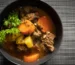 Crockpot beef stew with tender beef, carrots and potatoes in a dark bowl topped with parsley