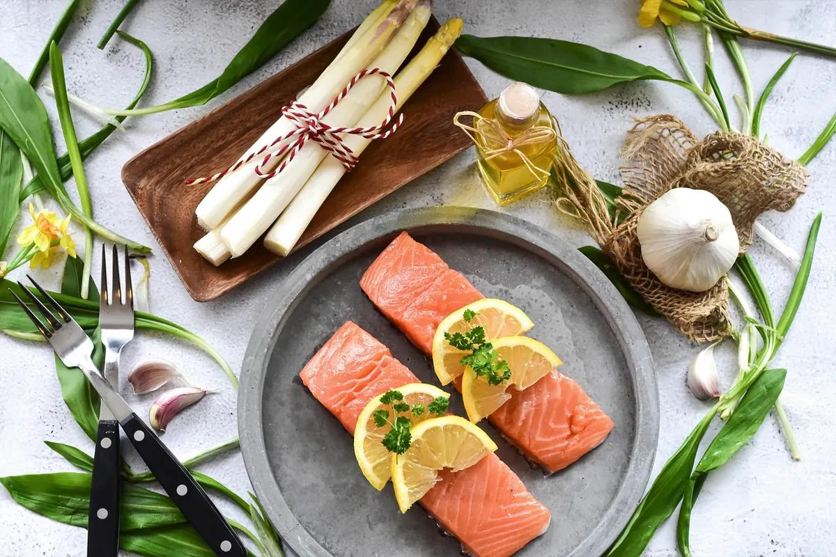 Raw salmon fillets with lemon slices, garlic and white asparagus on a gray plate