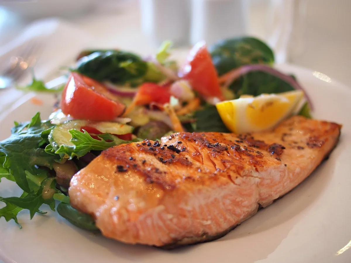 Cooked salmon fillet served with a fresh green salad, tomatoes and lemon