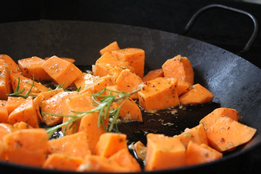 Diced sweet potatoes cooking in a pan with rosemary