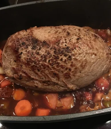 Seared beef roast braising with carrots in a dark roasting pot, similar to this chuck roast in the oven