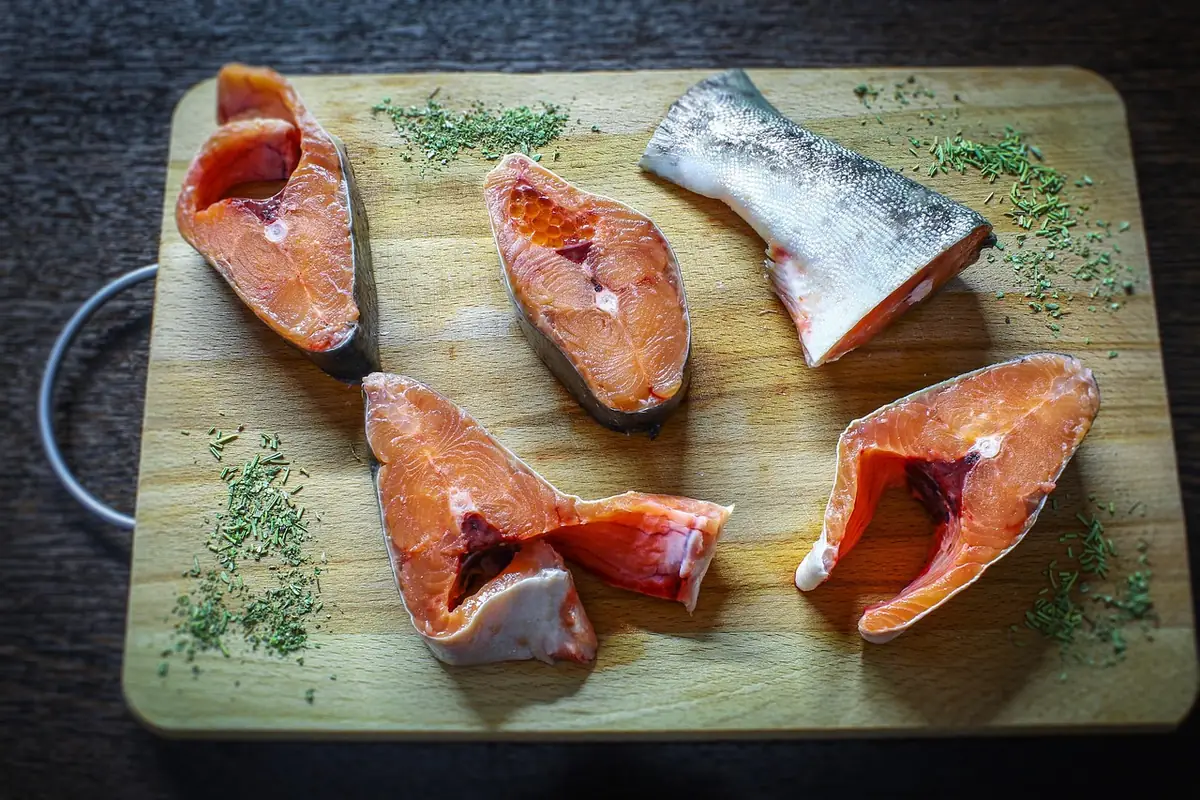 Raw salmon steaks and a tail piece on a wooden cutting board with dried dill