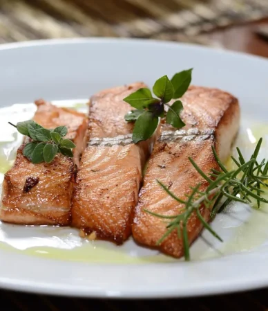 How to cook salmon: three seared salmon fillets with rosemary and olive oil on a white plate