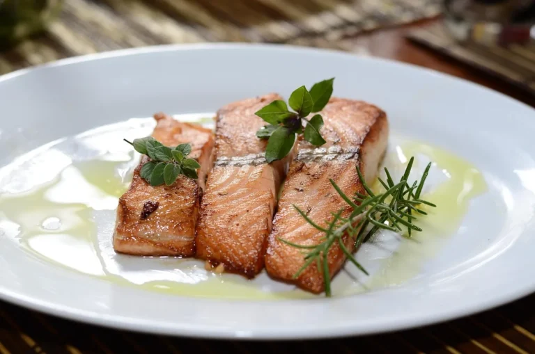 How to cook salmon: three seared salmon fillets with rosemary and olive oil on a white plate
