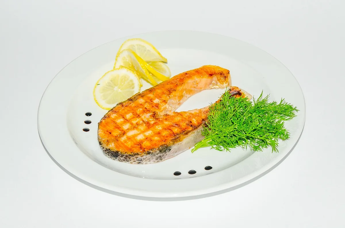 Grilled salmon steak with lemon slices and fresh dill on a white plate