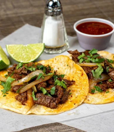 Grilled steak tacos with onions, cilantro and lime on corn tortillas, similar to tacos made with this skirt steak marinade