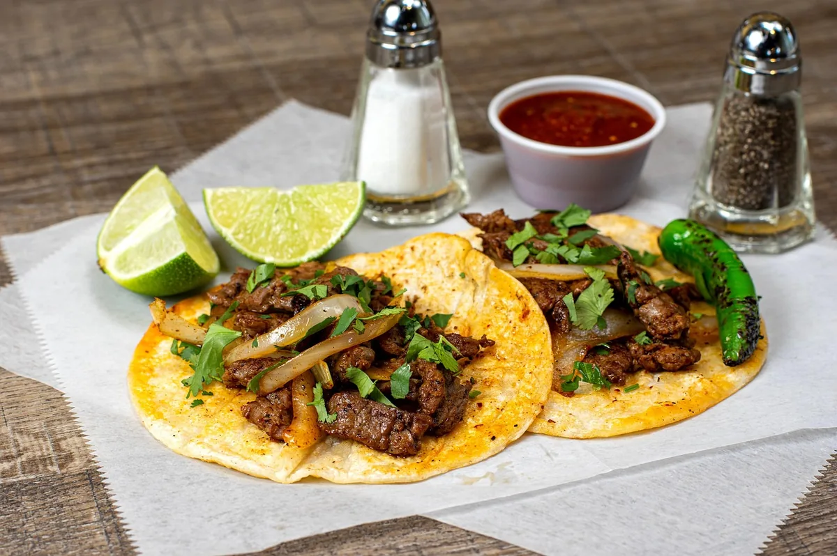Grilled steak tacos with onions, cilantro and lime on corn tortillas, similar to tacos made with this skirt steak marinade