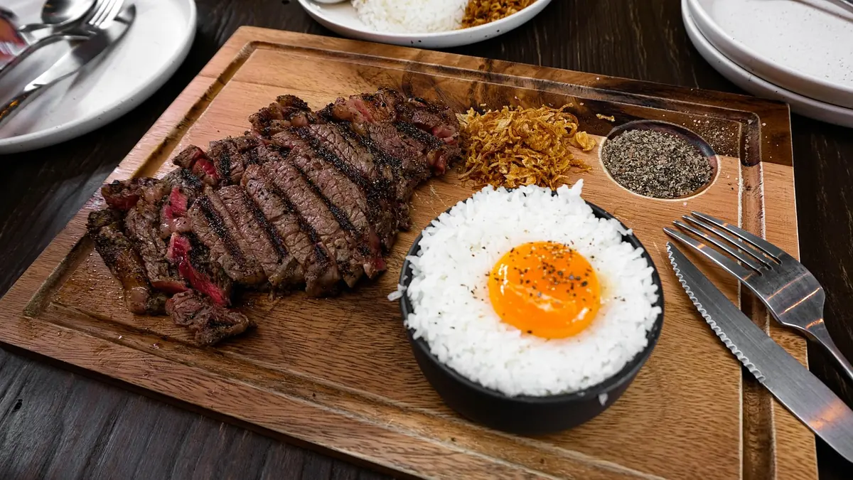 Grilled steak sliced across the grain on a wooden board, served with rice