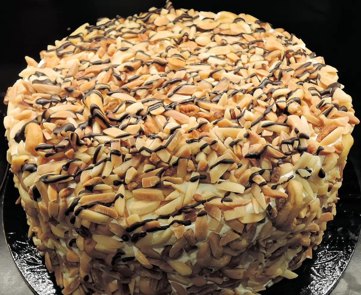 Tall round layer cake covered in toasted nuts with a chocolate drizzle, similar to this german chocolate cake recipe