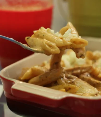 Cheesy baked penne being scooped from a red baking dish, similar to this chicken bacon ranch casserole