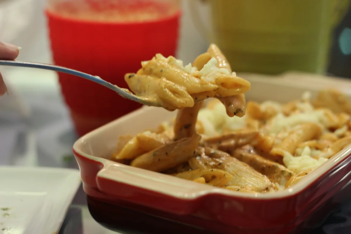 Cheesy baked penne being scooped from a red baking dish, similar to this chicken bacon ranch casserole