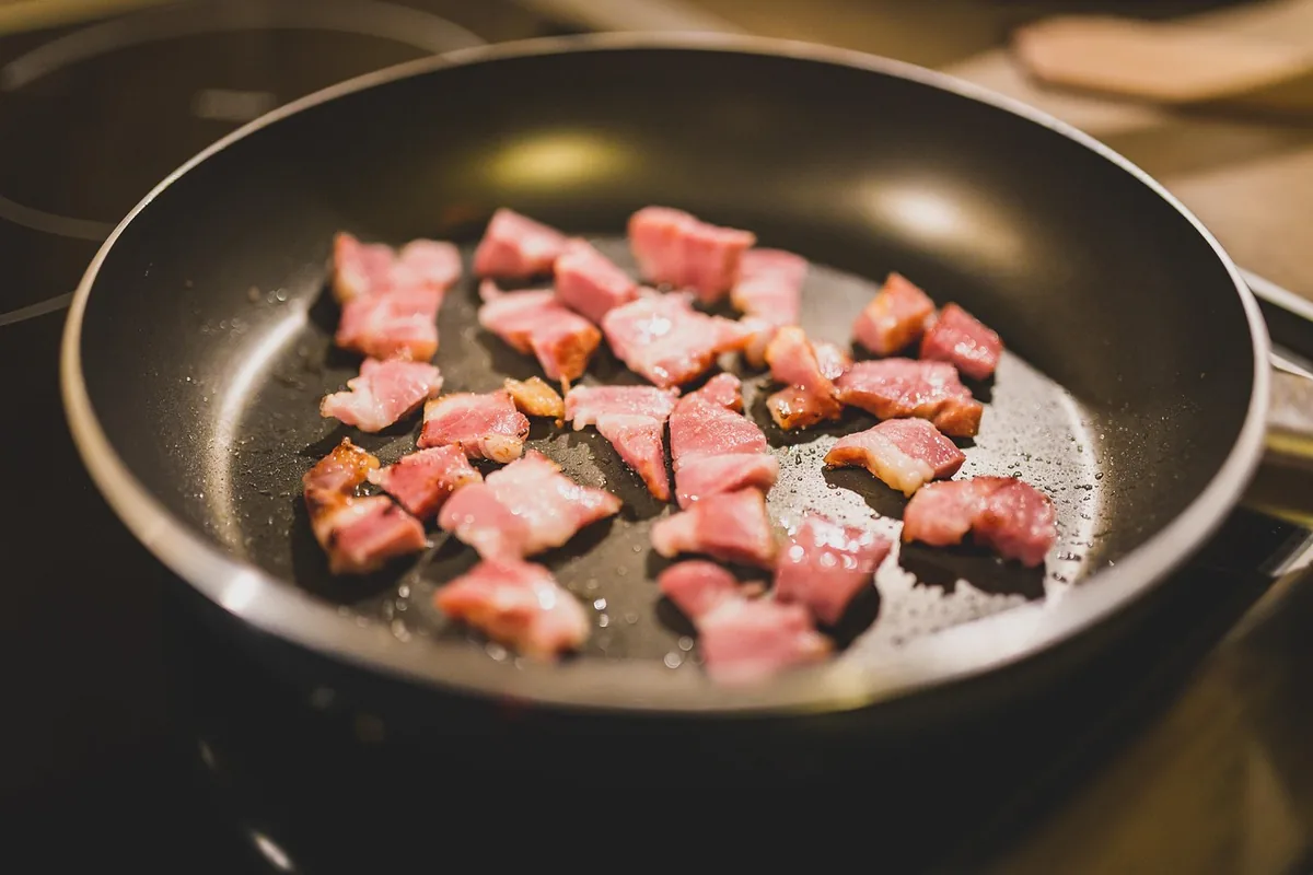 Diced bacon pieces cooking in a nonstick skillet for the casserole