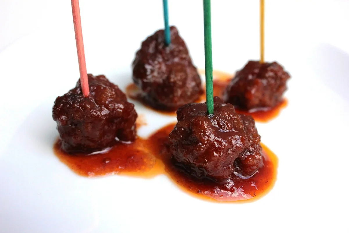 Glazed meatballs on colorful toothpicks with a sticky sauce, served as an appetizer