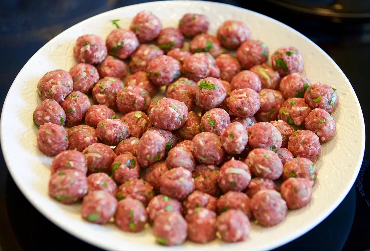 Raw ground beef meatballs with parsley rolled to the same size on a white plate, ready to air fry