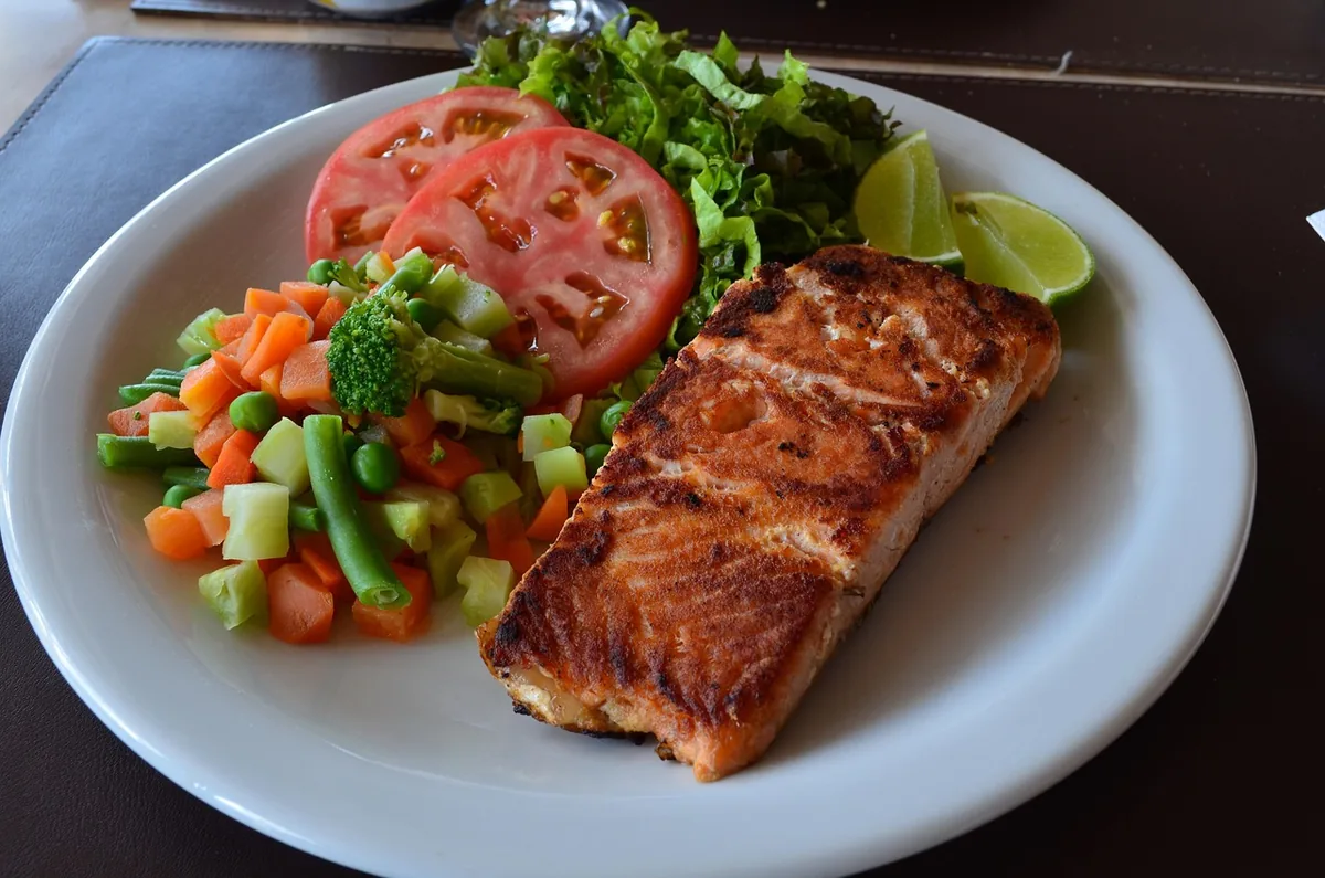 Golden oven baked salmon fillet served with mixed vegetables, tomato salad and lime