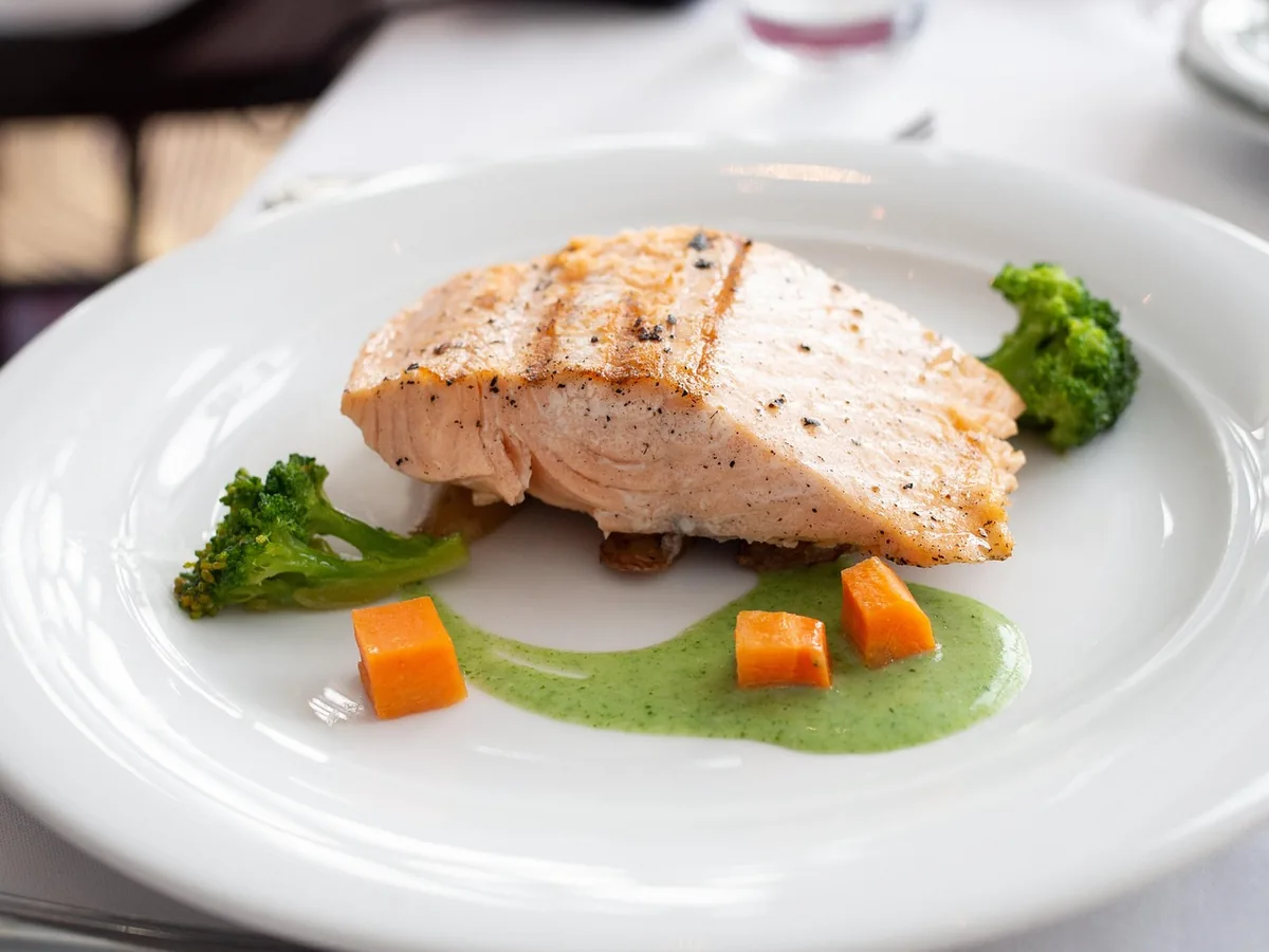 Opaque, flaky salmon fillet on a white plate with broccoli, showing baked salmon cooked through
