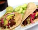 Two steak tacos with avocado, pickled red onion and lime on corn tortillas, similar to this steak tacos recipe