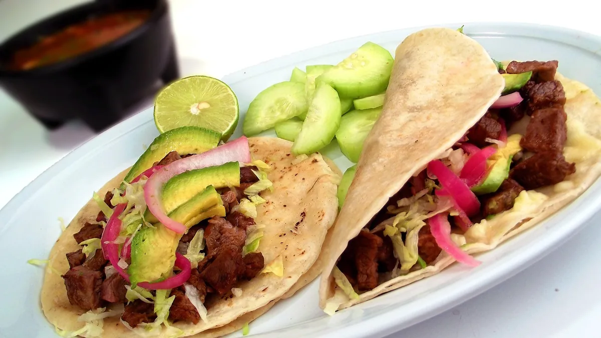 Two steak tacos with avocado, pickled red onion and lime on corn tortillas, similar to this steak tacos recipe