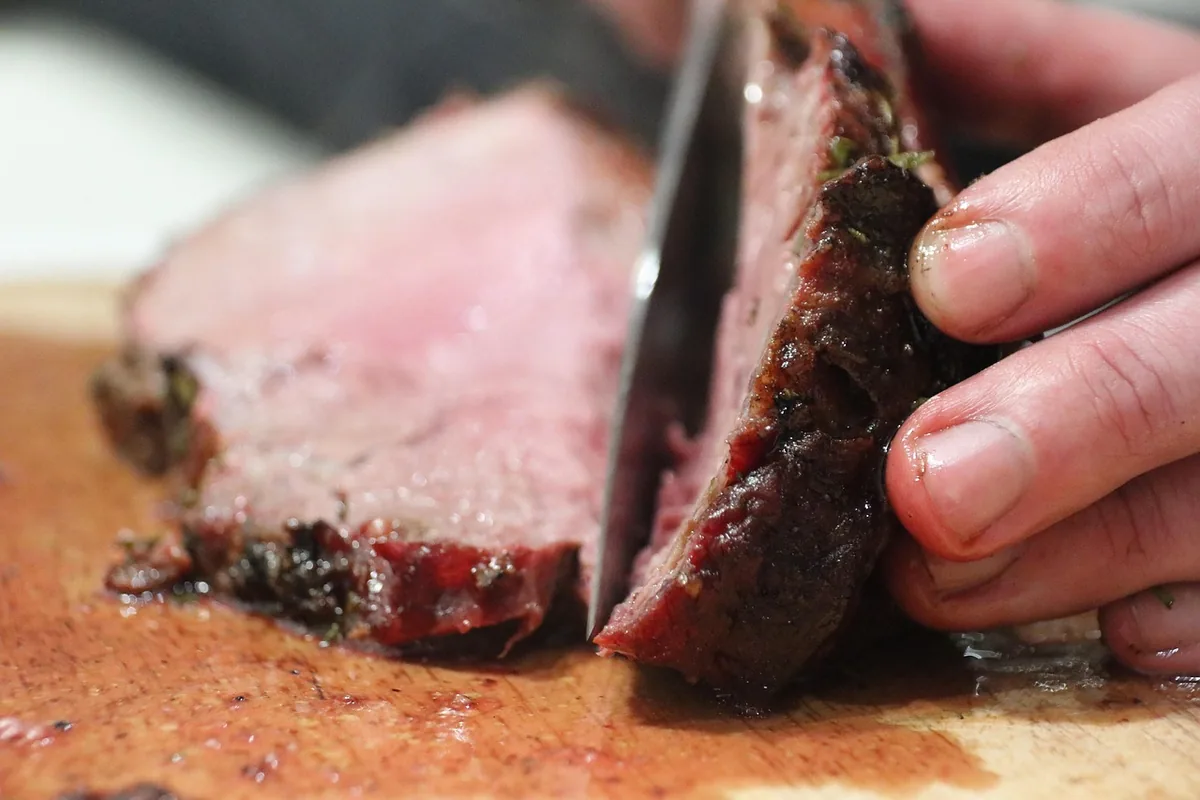 Slicing cooked beef thin against the grain on a wooden board, similar to slicing flank steak for tacos