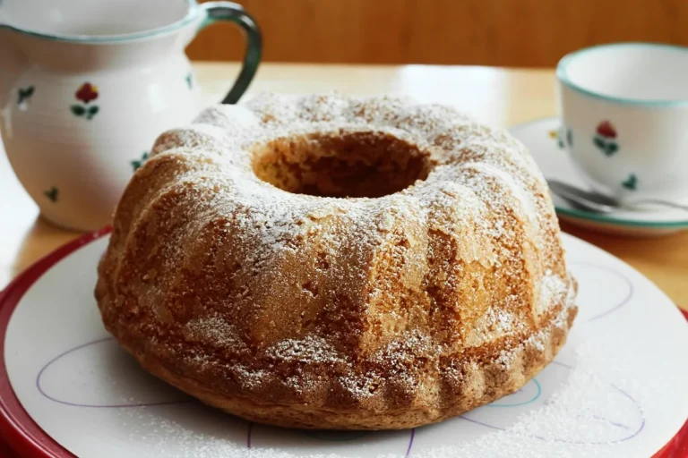 Golden Bundt cake dusted with powdered sugar on a plate, similar to this buttermilk pound cake recipe