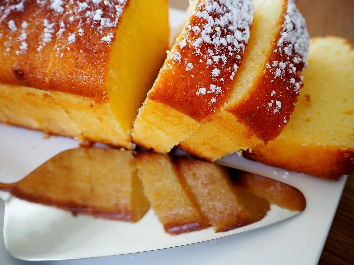 Sliced golden loaf cake dusted with powdered sugar, similar to a buttermilk pound cake baked in a loaf pan