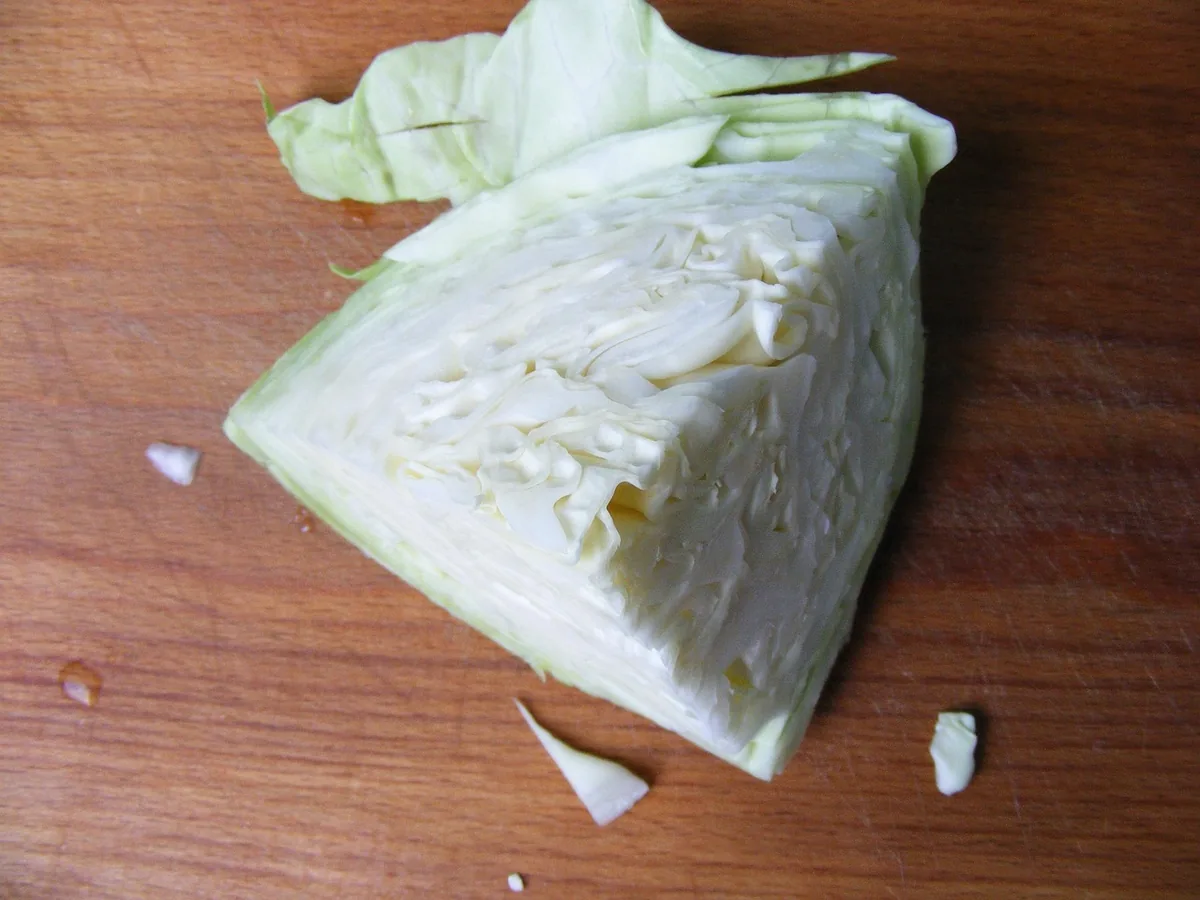 Quarter of green cabbage on a wooden board with the core cut out, ready to chop into 1-inch pieces