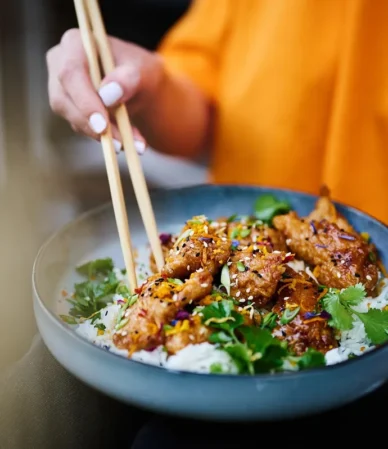 Glazed sesame-topped pieces over rice in a blue bowl with chopsticks, similar to this salmon bowl recipe